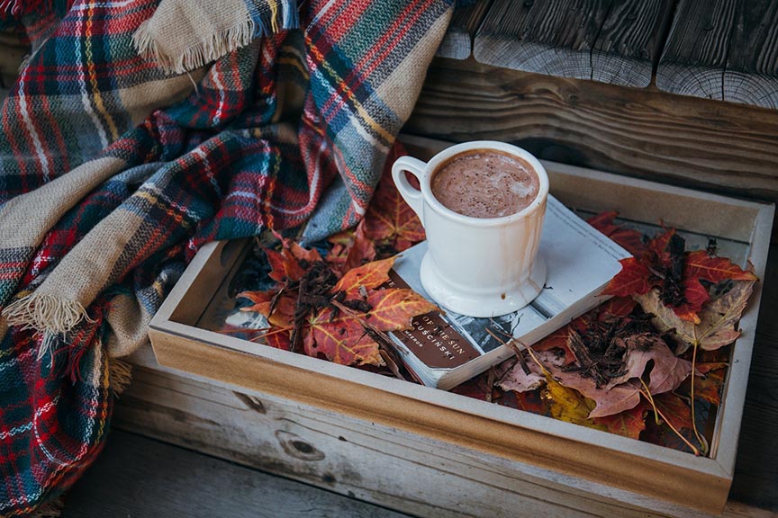 Hot coffee with a blanket and a book in a fall setting